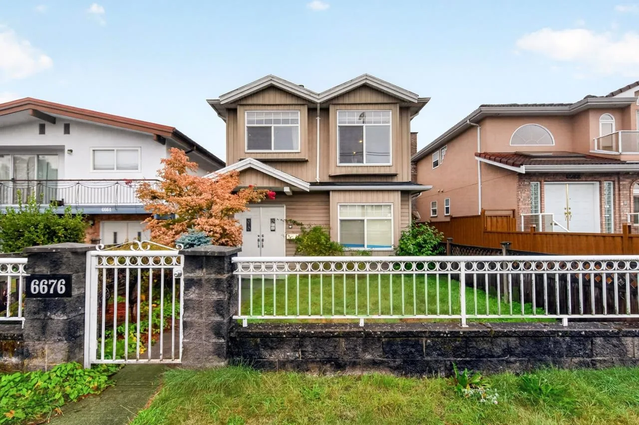 Front exterior of 6676 Victoria Drive: a two-storey half duplex with a fenced front yard